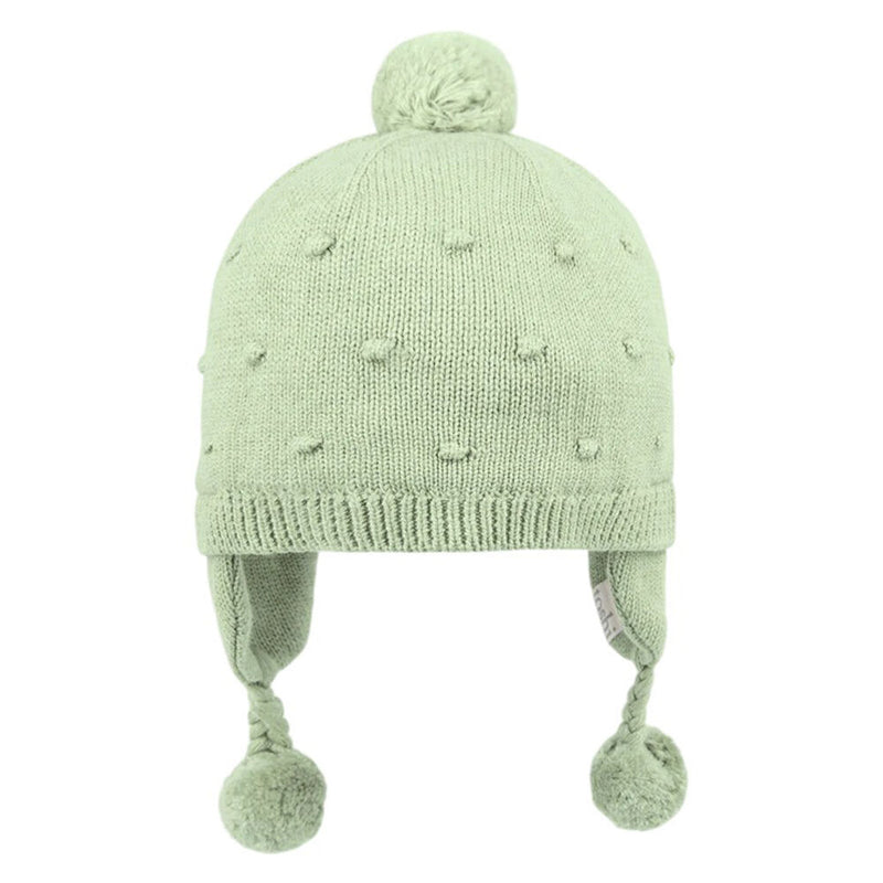 The Toshi Organic Earmuff Popcorn/Matcha is a light green baby beanie with ear flaps, braided tassels ending in pom-poms, and textured dots—perfect for keeping your little one cozy and warm in winter.