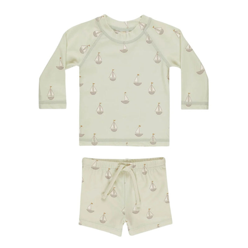 The Quincy Mae Finn Rashguard + Short Set Sailboats is a two-piece children’s set with long sleeves and shorts in light cream, featuring a sailboats print in soft beige and brown tones.