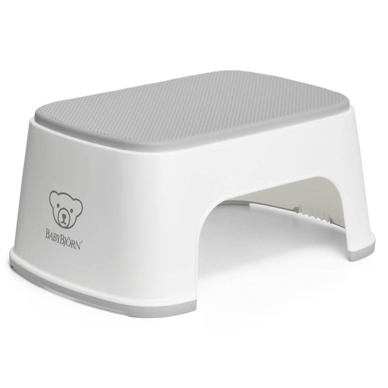 The BabyBjorn Step Stool is a white plastic children's stool with a gray non-slip top and bear logo, featuring rounded edges and short legs for added safety.