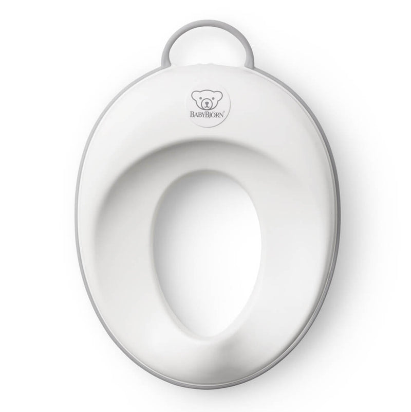 A white and gray BabyBjorn Potty Toilet Trainer by BabyBjorn, featuring an ergonomic handle and bear logo above the seat opening, is seen from above on a white background.