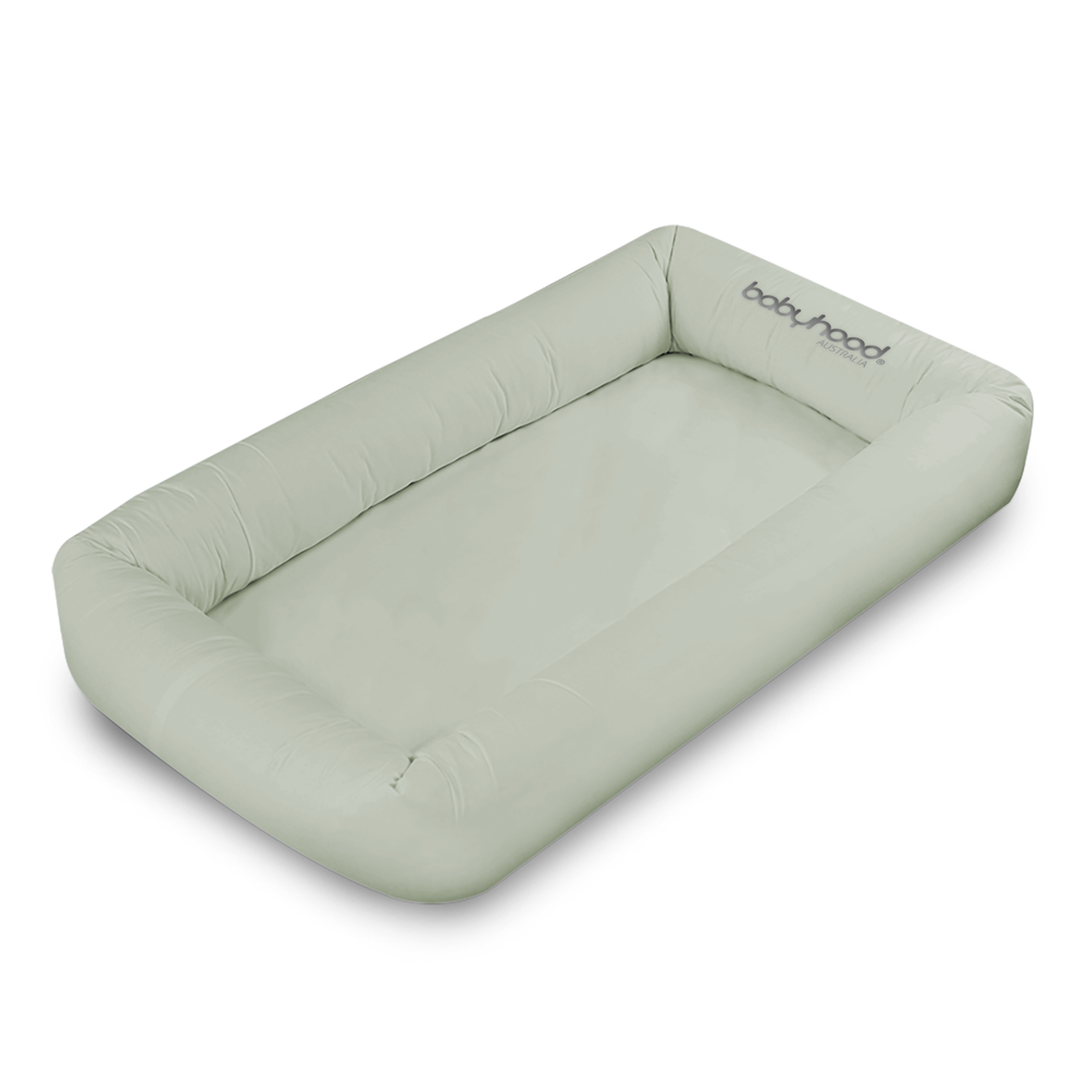 The Babyhood Original Cosy Crib is a light gray, rectangular baby pod with raised cushioned sides and "Babyhood" printed in the top right corner, designed for safe sleep and comfort.