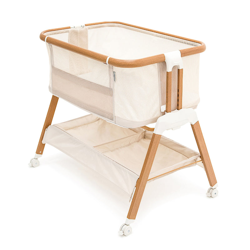 The BabyRest Alfie2 Bedside Bassinet in Beige Walnut by BabyRest features a modern light wood frame, white mesh sides for safety, a lower storage shelf, and four white wheels—ideal for co-sleeping and keeping your baby close and comfortable.