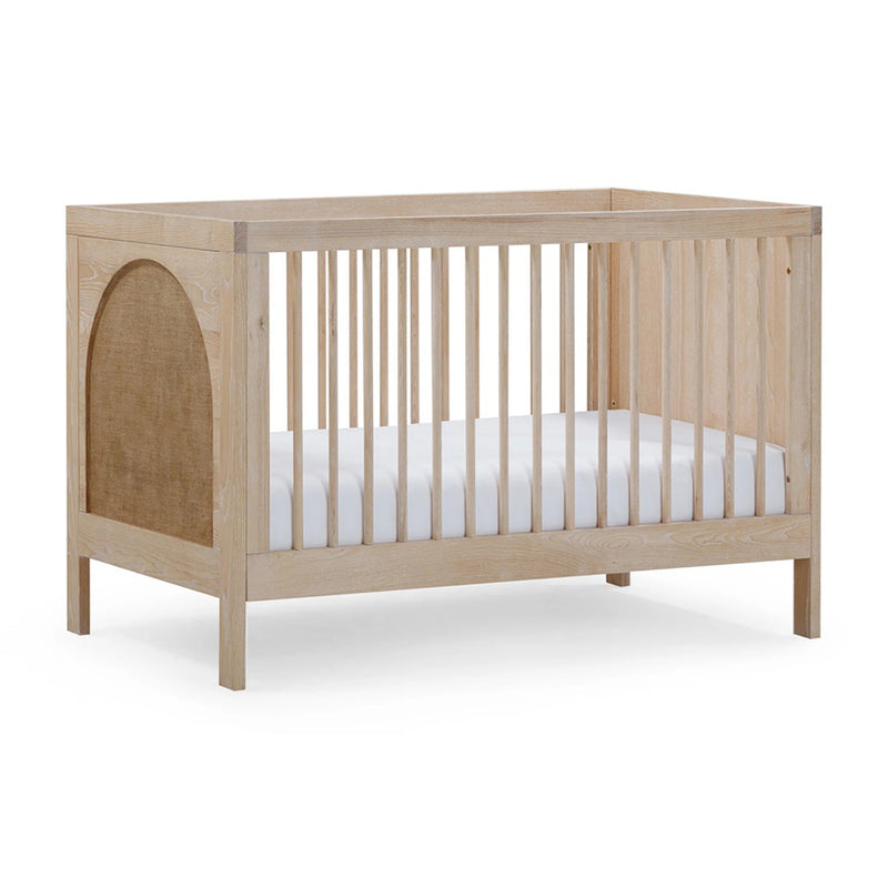 The BabyRest Grove Cot by BabyRest is a light European Ash cot with vertical side slats, a solid end panel featuring a beige fabric insert, and includes a white mattress. This 3-in-1 cot offers a simple, modern design.