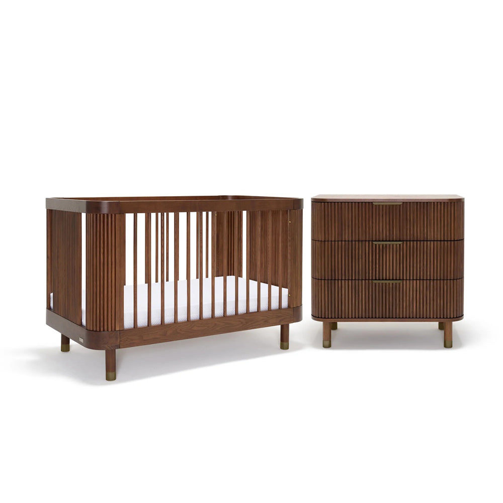 The BabyRest Juno Cot Walnut + Juno Dresser Walnut + DuoCore Mattress Nursery Package features modern, rounded designs in a dark walnut finish, including a cot with vertical slats and a matching three-drawer dresser against a white background.