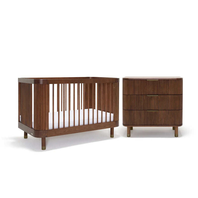 The BabyRest Juno Cot Walnut + Juno Dresser Walnut + DuoCore Mattress Nursery Package features modern, rounded designs in a dark walnut finish, including a cot with vertical slats and a matching three-drawer dresser against a white background.