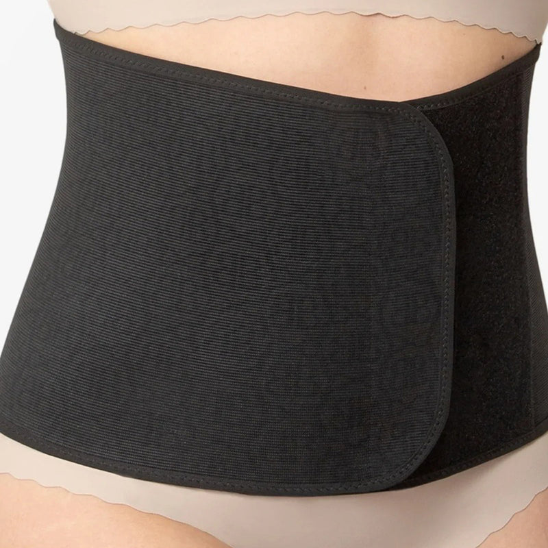 A person wearing a beige undergarment and the Belly Bandit Original Postpartum Belly Wrap in black, by Belly Bandit, wrapped snugly around their midsection.