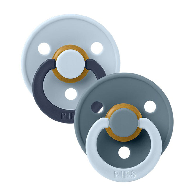 The Bibs Dummies Fusion Colour Baby Blue Petrol Mix includes two BPA-free round pacifiers with ring handles—one in baby blue and navy, the other in dark gray with a light blue handle. Both feature circular shields with ventilation holes.