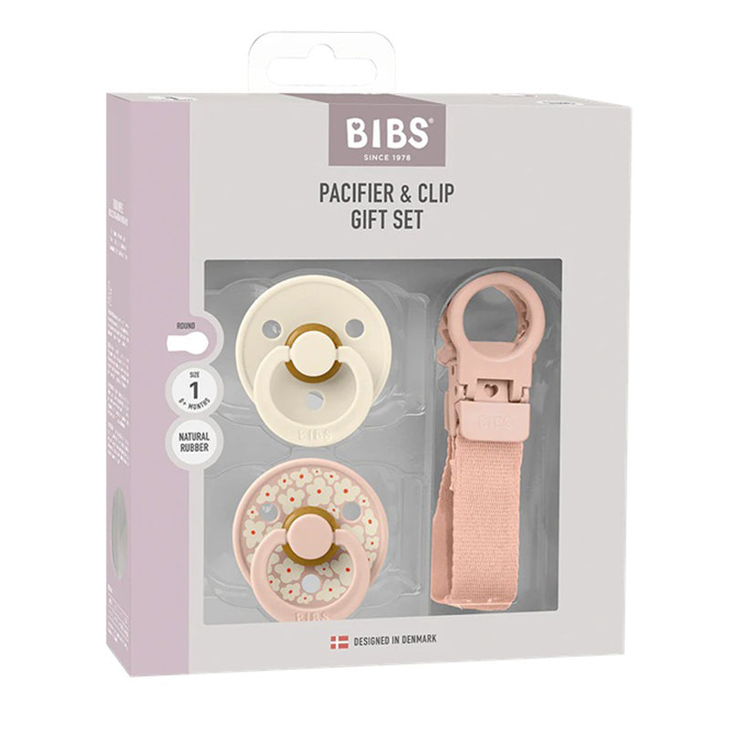 The Bibs Dummies Pacifier & Loop Clip Gift Set Size 1 Blush includes two round pacifiers—one solid cream, one floral—and a pink loop clip, all visible through the packaging window. Brand: Bibs Dummies.