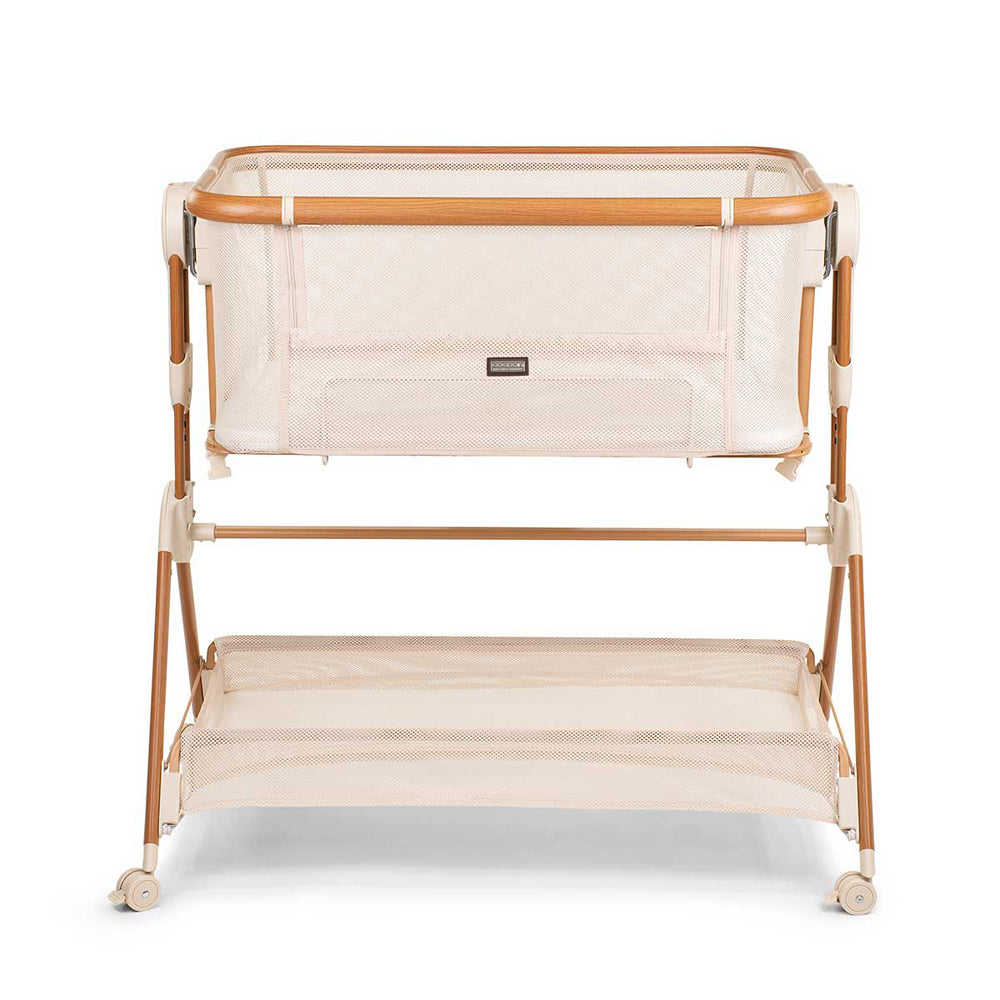 The Cocoon Breeze Co Sleeper Bassinet by Cocoon features a modern beige design, wooden frame, mesh sides, lower storage shelf, and four legs with rear wheels for easy mobility—ideal for keeping your baby close and comfortable at night.