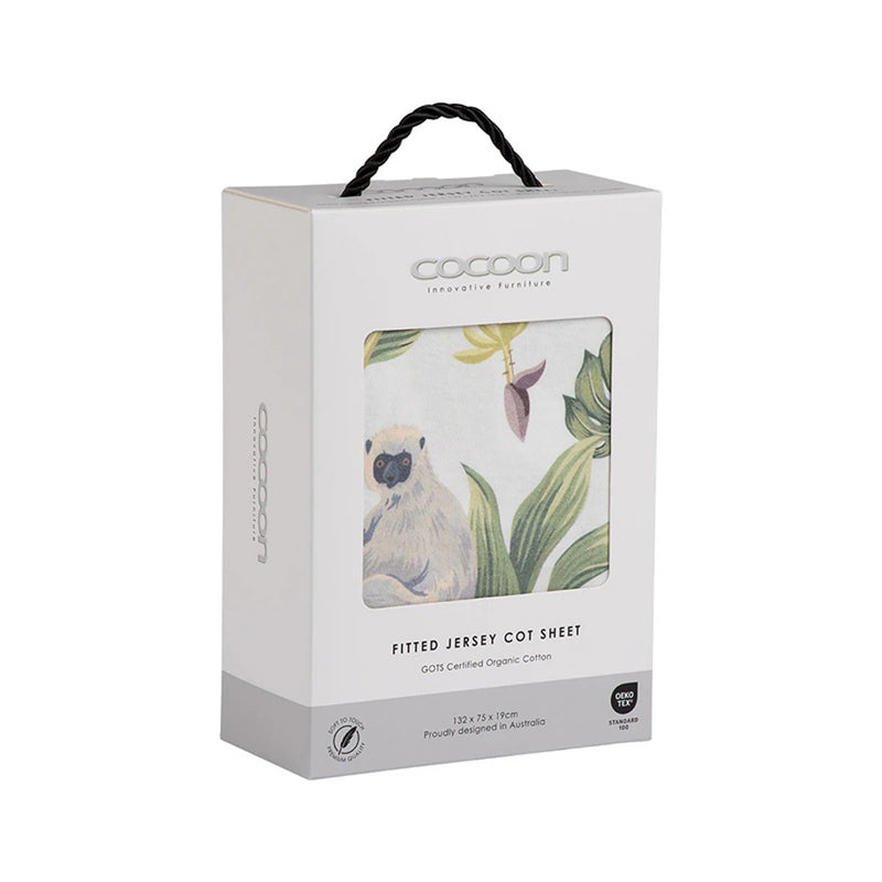 A white box of Cocoon Fitted Sheet Cot Tropicana with a window displays its tropical cockatoo and leaf print. Featuring a black handle, the packaging highlights organic cotton, GOTS certification, and Australian design.