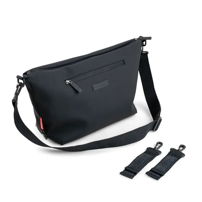 The Done By Deer Stroller Bag by Done By Deer is a sleek black crossbody bag with a zippered front pocket, adjustable shoulder strap, and two detachable padded attachments for baby essentials, shown beside a stroller on a white background.