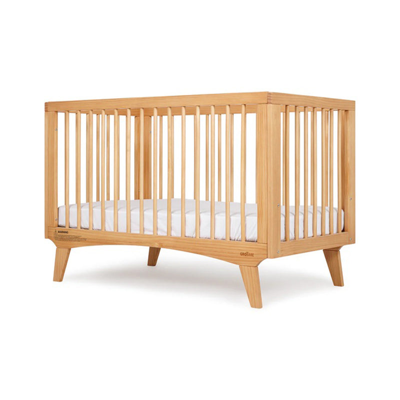The Grotime Mia Cot by Grotime, made from New Zealand Pine with vertical slats, angled legs, and a white mattress, is displayed against a plain white background.