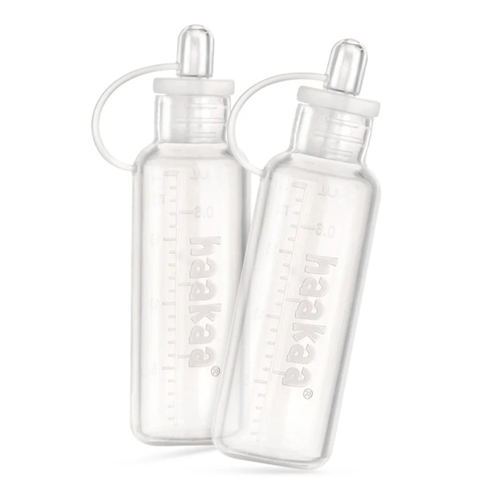 Two Haakaa Silicone Colostrum Collector Set Pre-Sterilised 20ml containers, branded with Haakaa, stand upright and slightly lean together on a white background.