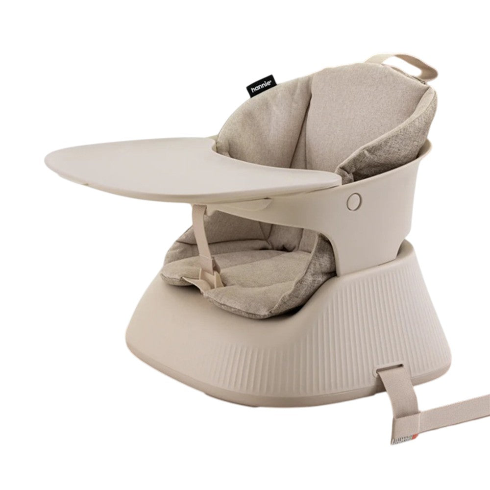 The Hannie Portable High Chair by Hannie is a beige baby booster seat with a cushioned backrest, safety harness, detachable tray, and securing strap. Its modern, minimalist design is perfect for mealtime at home or on the go.
