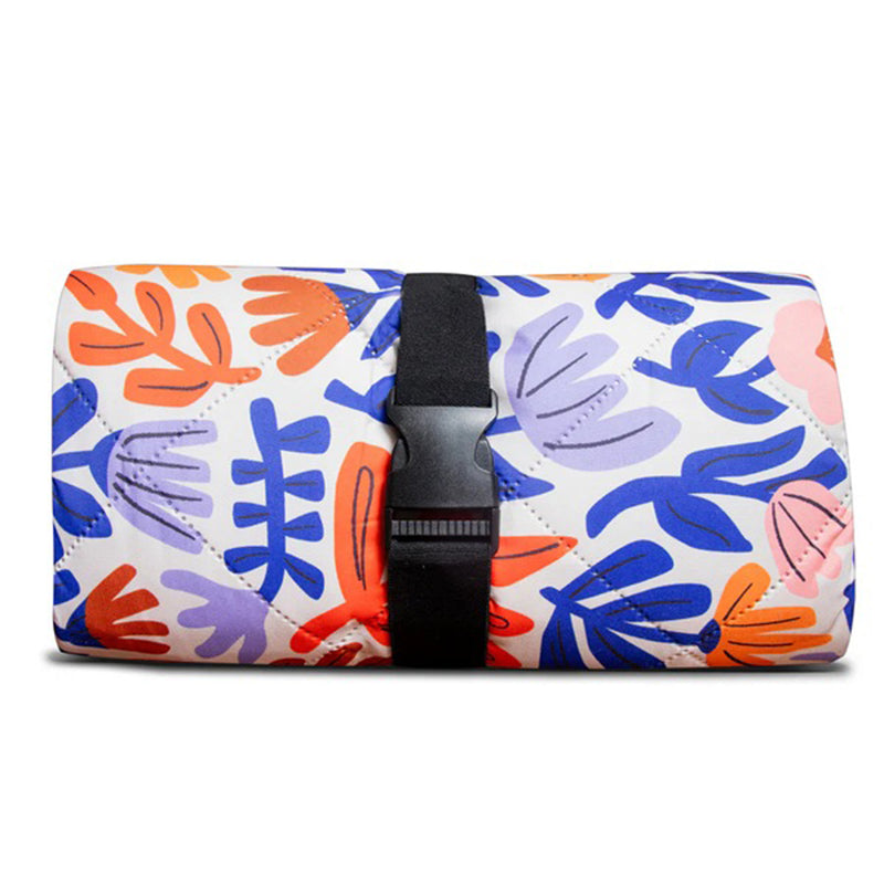 The IZIMINI Willow Picnic Rug by IZIMINI features a vibrant floral pattern in orange, purple, and blue. Easily rolled up and secured with a black strap and buckle, this machine-washable rug is perfect for outdoor adventures.