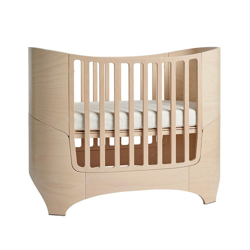 The Leander Classic Cot by Leander features a modern Scandinavian design with light wood, curved edges, and vertical slats. Shown here with a white mattress, this convertible baby cot adds minimalist style to any nursery.