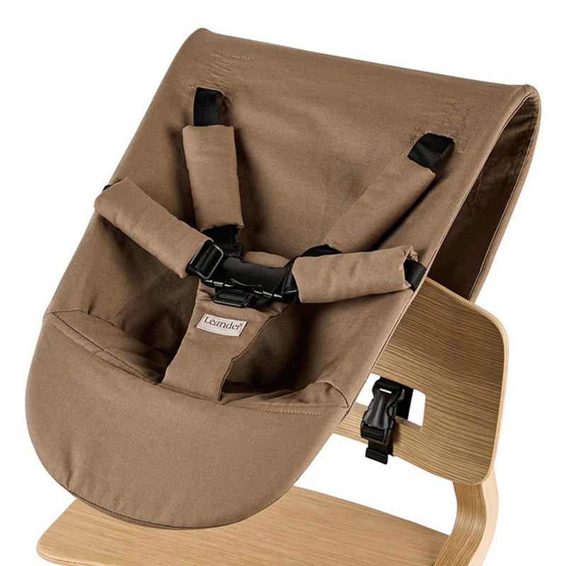 The Leander Louie Newborn Seat by Leander is a brown organic cotton baby seat with shoulder, waist, and crotch straps plus black buckles for safety. Designed with a light wooden frame, it’s the perfect accessory for your Leander highchair.