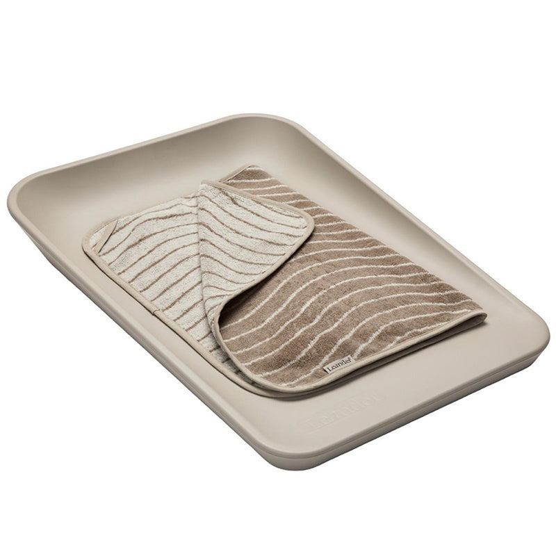 The Leander Matty Change Top Bundle by Leander holds a striped, reversible tan and white changing pad. The waterproof mat is partially folded to display both sides of the fabric, combining style with practicality.