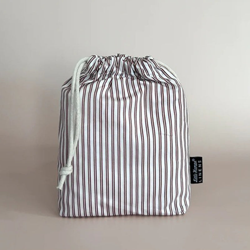 A drawstring bag made from soft, breathable organic cotton, repurposed from a Little Humans Linens Waterproof Bassinet Sheet 81x41 by Little Humans Linens, with white fabric featuring red and brown stripes, a white drawstring closure, and a black side tag.