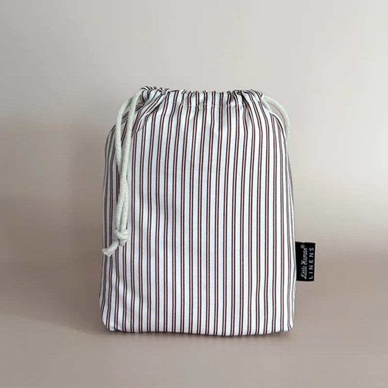 A maroon and white striped drawstring bag by Little Humans Linens sits upright against a light background, featuring a black tag—perfect for carrying the Little Humans Linens Waterproof Change Pad / Euro Bassinet Sheet 85x51.