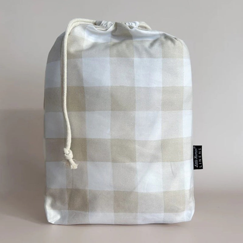 A beige and white checkered drawstring bag stands upright against a plain background, featuring a black tag on the right. Ideal for carrying essentials like the Little Humans Linens Waterproof Cot Sheet by Little Humans Linens.