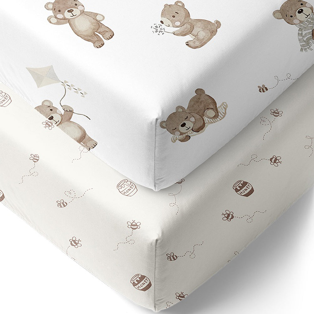 The Living Textiles Cot Fitted Sheet Cuddly Bear by Living Textiles includes two crib sheets: one with playful brown teddy bears on white, and a second with smaller bears, bees, and honey pots—breathable baby bedding for comfy nursery essentials.