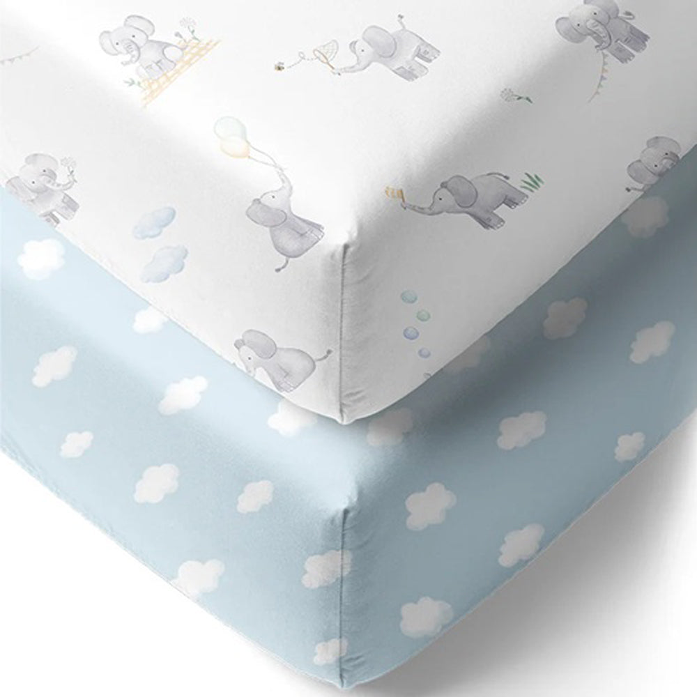 The Living Textiles Cot Fitted Sheet Elephant Playtime features a white, breathable sheet with gray elephants holding balloons and kites, plus a light blue sheet with white clouds—ideal nursery bedding from Living Textiles.