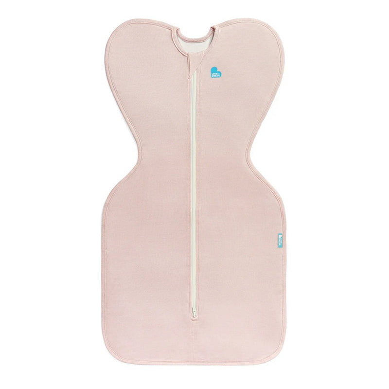 The Love To Dream Swaddle Up 0.2T Stretch Cotton Blush by Love To Dream is a light pink, wing-shaped baby swaddle with a central white zipper and blue heart logo, designed for arms up self-soothing, shown flat on a white background.
