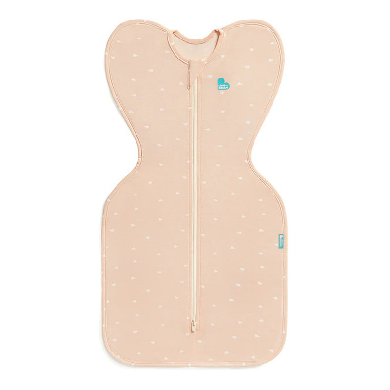 The Love To Dream Swaddle Up 0.2T Viscose From Bamboo Hearts Blush features a peach hue with white heart prints, wing-like shoulders, a central zipper, and supports the healthy Arms Up sleeping position for your baby.