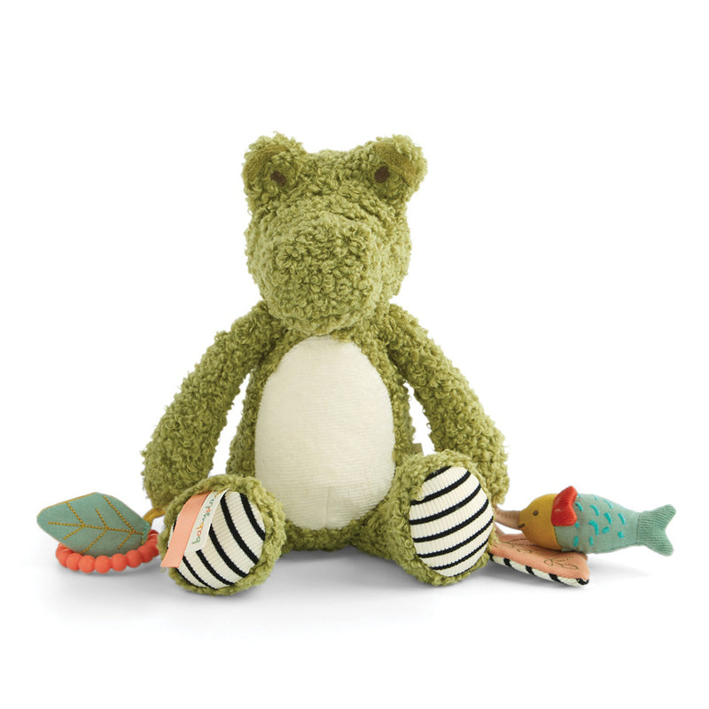 The Mamas & Papas Activity Toy Cody Crocodile plush features a white belly, striped feet, and sensory accessories—a leaf, fish, bird, and teething ring—set against a white background.