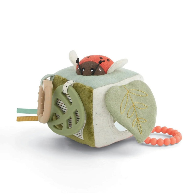 The Mamas & Papas Mini Activity Cube is a soft sensory toy featuring a plush ladybug, green teething elements, embroidered leaf flaps, colorful tags, and an orange beaded ring—ideal as a pram toy for on-the-go fun.