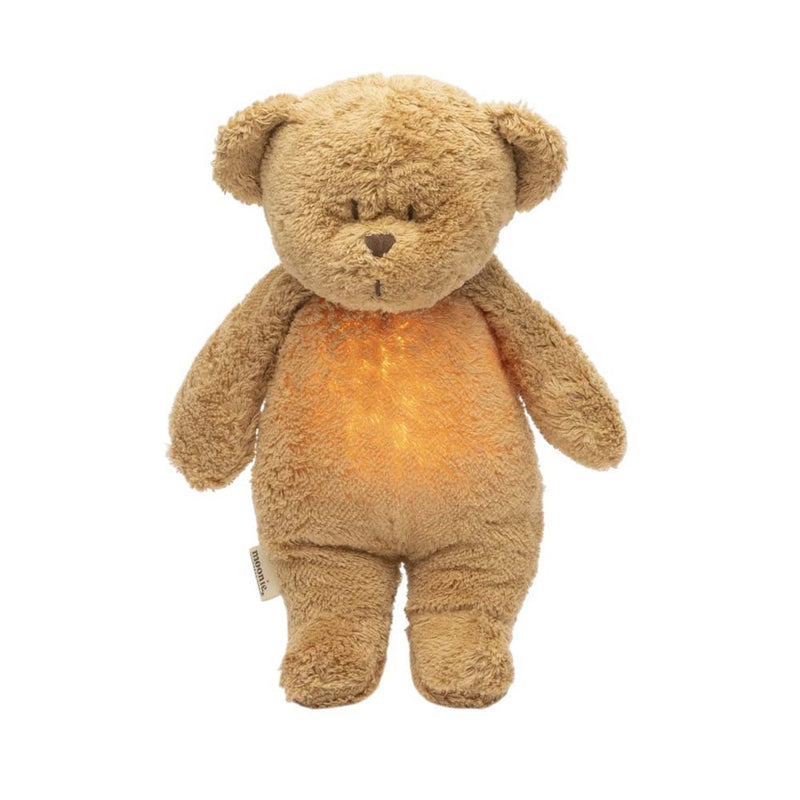 The Moonie Organic Humming Bear Cappuccino by Moonie is a light brown plush bear with small round ears and a soft, slightly worn texture. It features a gentle night light in its belly, making it an ideal baby sleep aid.