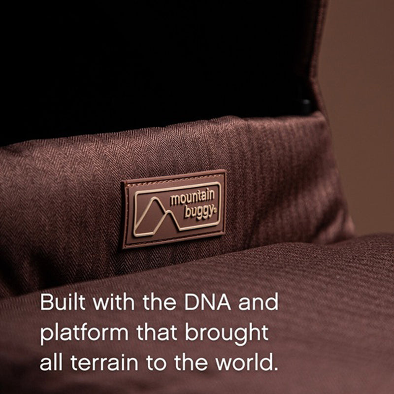 Close-up of the brown fabric seat on the Mountain Buggy Carrycot Plus for Urban Jungle V4, featuring the Mountain Buggy logo patch and modular seat design with newborn lie-flat functionality.