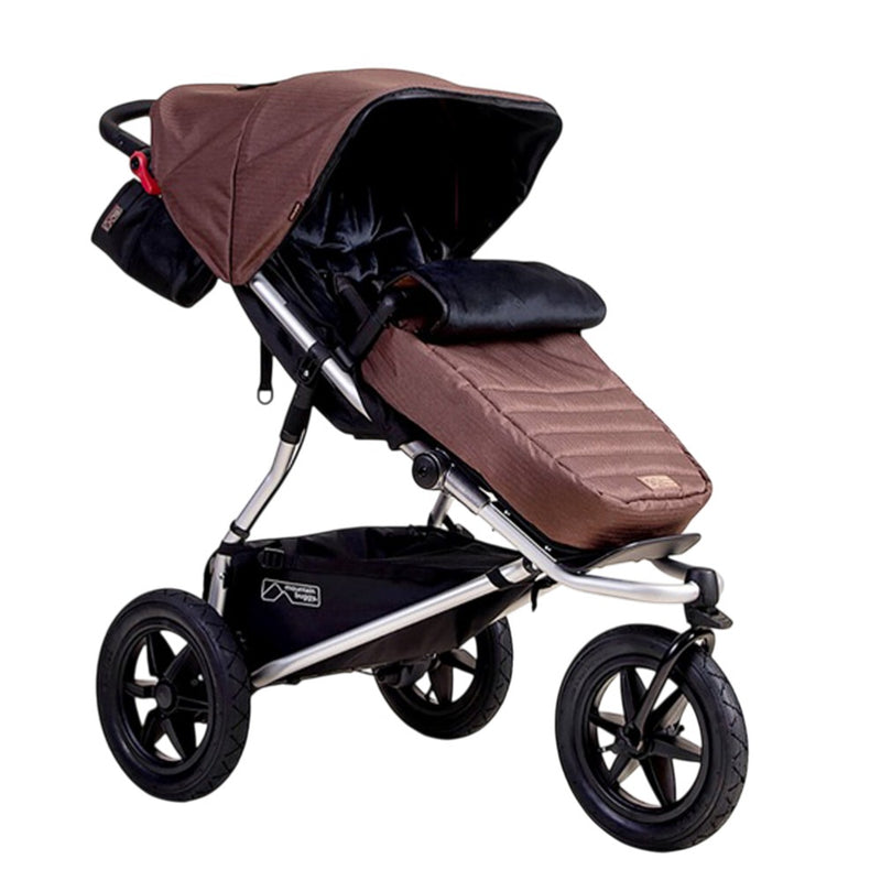 A brown three-wheeled stroller with sun canopy, black storage pouch, reclining seat, and large black wheels is shown against a white background featuring the Mountain Buggy Footmuff accessory for extra comfort.