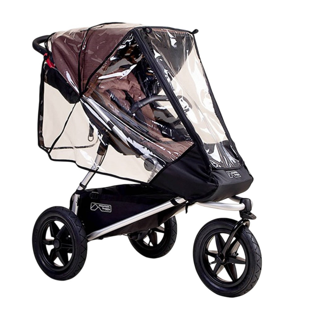 A Mountain Buggy Urban Jungle & Terrain Storm Cover, shown on a black stroller with large wheels, shields the seat and handlebar area. The empty stroller is displayed against a white background.