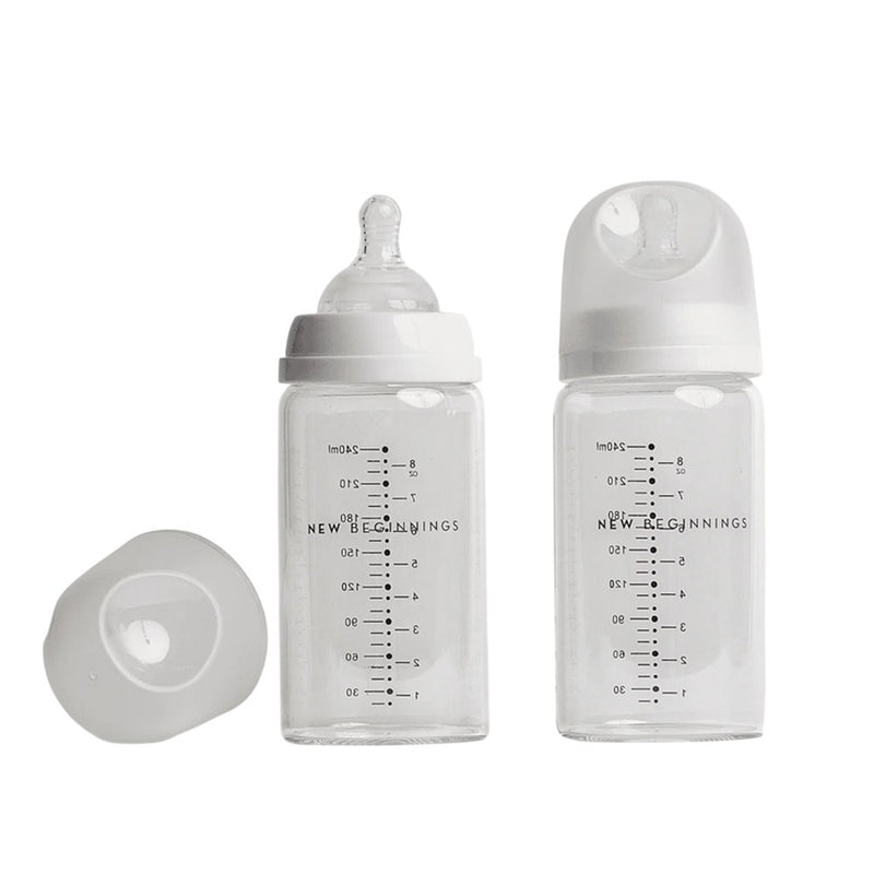 The New Beginnings Classic Glass Bottle 240ml Twin by New Beginnings includes two clear bottles with white lids and measurement markings—one with a nipple, one capped—plus an extra cap for a practical, safe feeding solution.