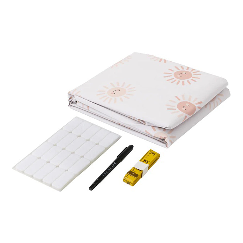 The Porta Fox Cut-to-Size Blackout Blind Sunny Smiles kit includes white fabric with a sun pattern, adhesive rectangles, a black marker, and a yellow measuring tape—ideal for creating your own nursery blackout blind.