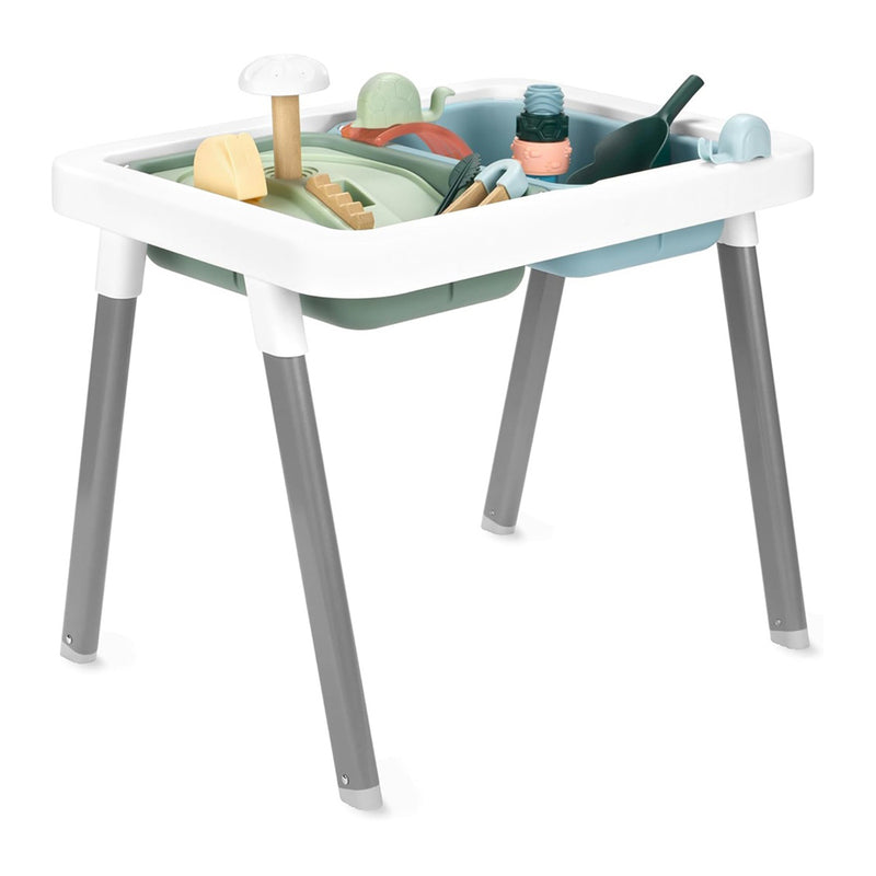 The Skip Hop Discoverosity 3-in-1 Sensory Table by Skip Hop is a white and gray toddler table with two compartments, filled with pastel toys—such as a mushroom, shovel, and bottle—designed for engaging sensory play against a white background.