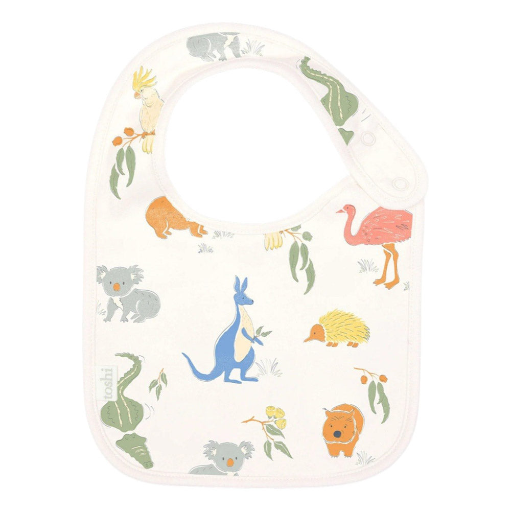 The Toshi Baby Bib Classic by Toshi is a white cotton bib with Australian animals—blue kangaroo, koala, pink emu, echidna, wombat, cockatoo—and green leaves. This cute adjustable bib keeps little ones comfortable and clean.
