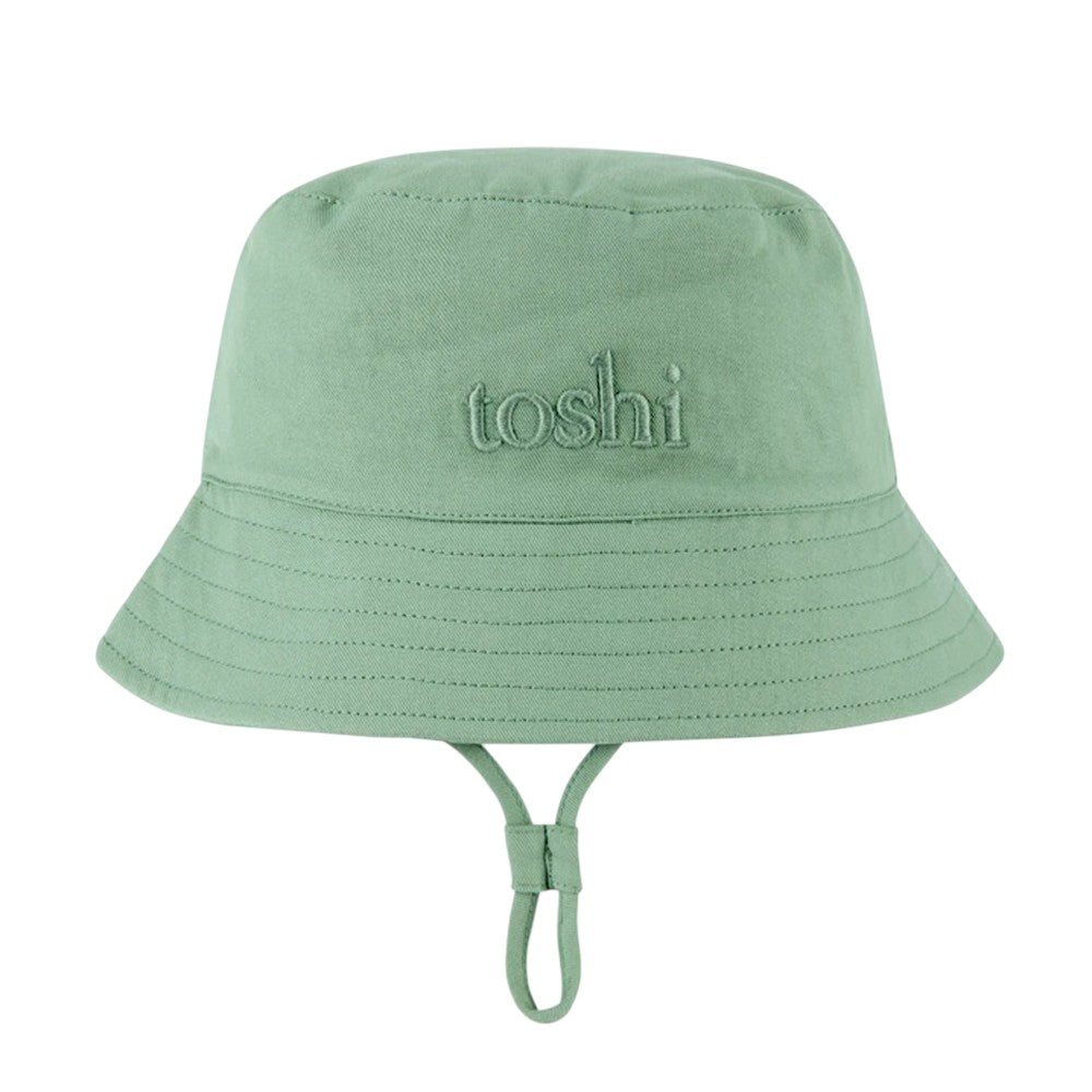 The Toshi Bucket Hat Billy Teal is a kids’ cotton bucket hat in light green with "toshi" embroidery, visible stitching, an adjustable chin strap, and UPF 50+ sun protection—perfect for sunny days.