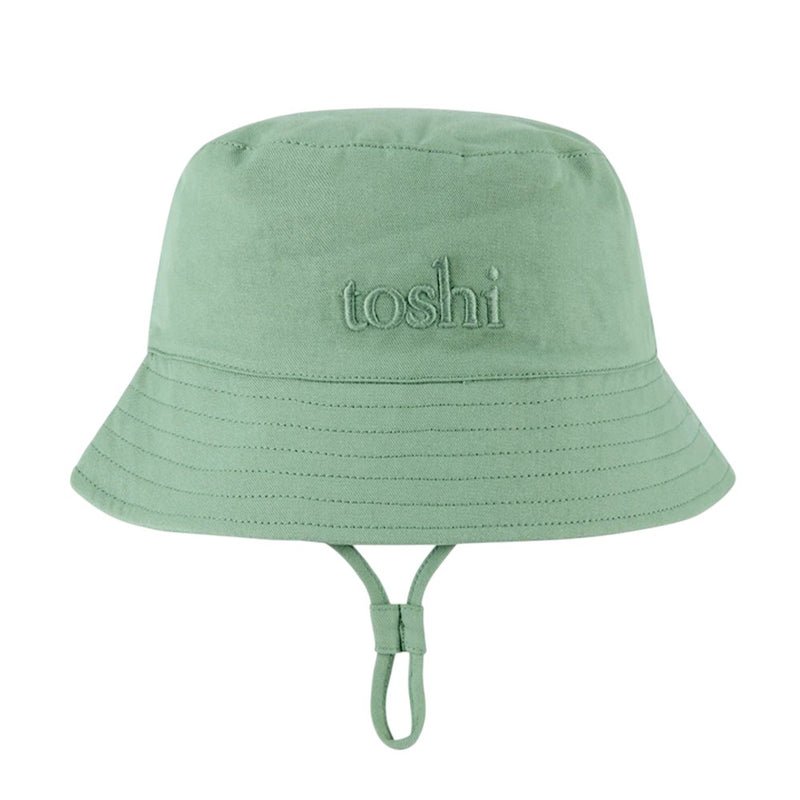 The Toshi Bucket Hat Billy Teal is a kids’ cotton bucket hat in light green with "toshi" embroidery, visible stitching, an adjustable chin strap, and UPF 50+ sun protection—perfect for sunny days.