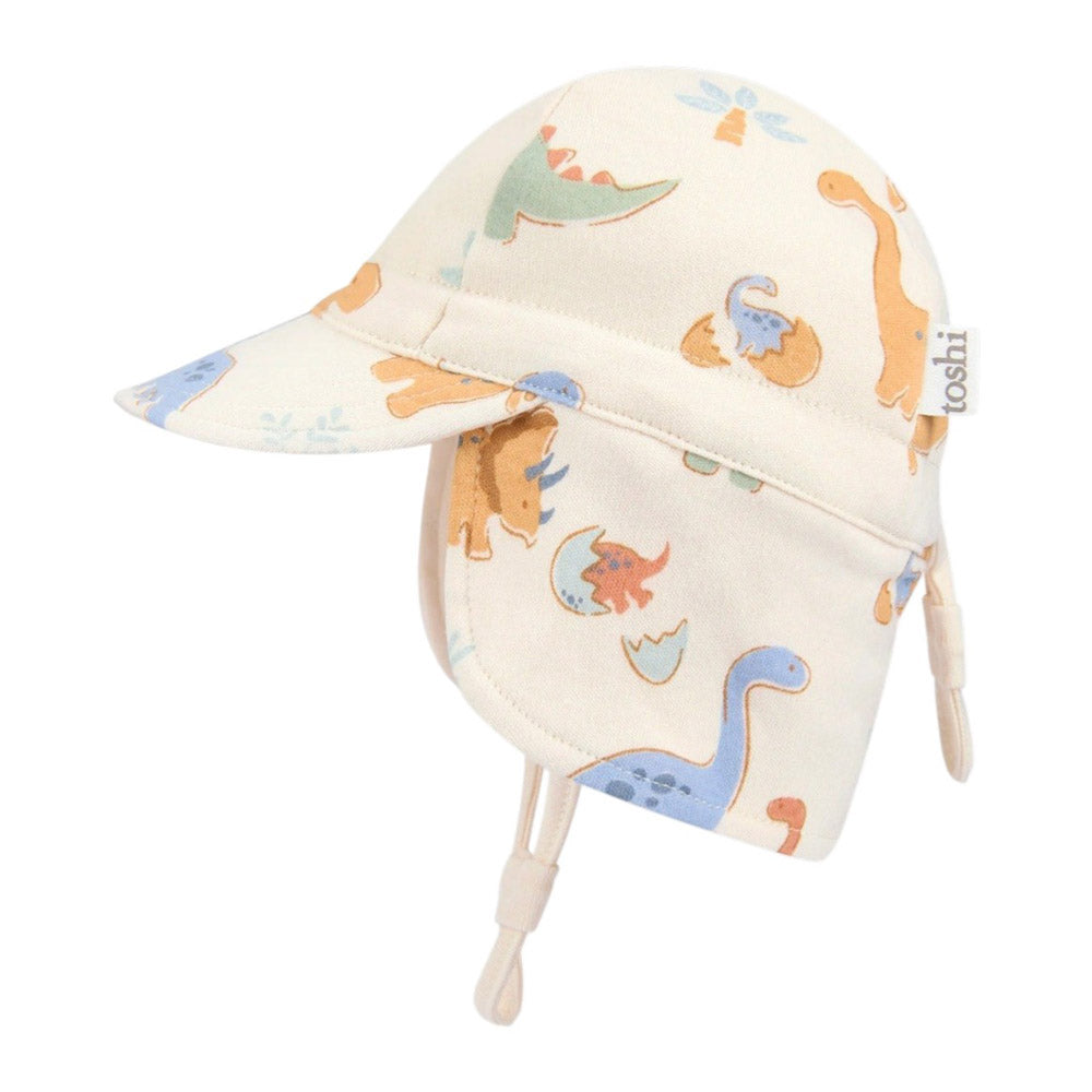 The Toshi Flap Cap Harvest Dino Bubs is a cream baby sun hat with a flap and chin straps, decorated with colorful cartoon dinosaurs and trees. Offering UPF 50+ protection, it keeps your little one safe in style.