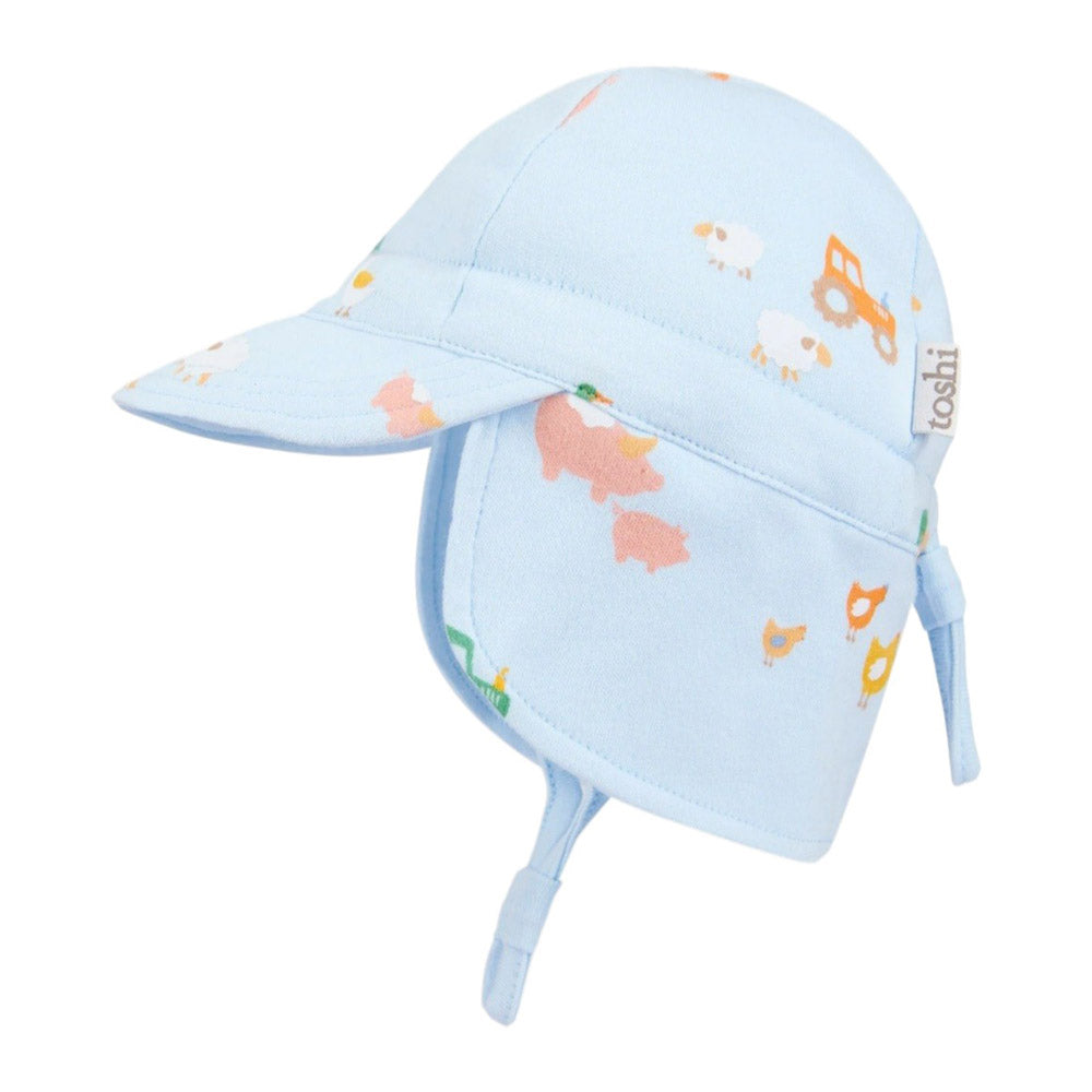 The Toshi Flap Cap Harvest Farm Buddies by Toshi is a light blue baby sun hat with UPF 50+ protection, neck flap, and chin straps, featuring pastel farm animals and tractors. Shown on a white background.