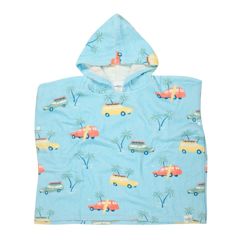 The Toshi Hooded Towel Paradise Swell Seekers Sky is a children’s blue cotton poncho with a fun print of cars, surfboards, and palm trees on a light blue background.