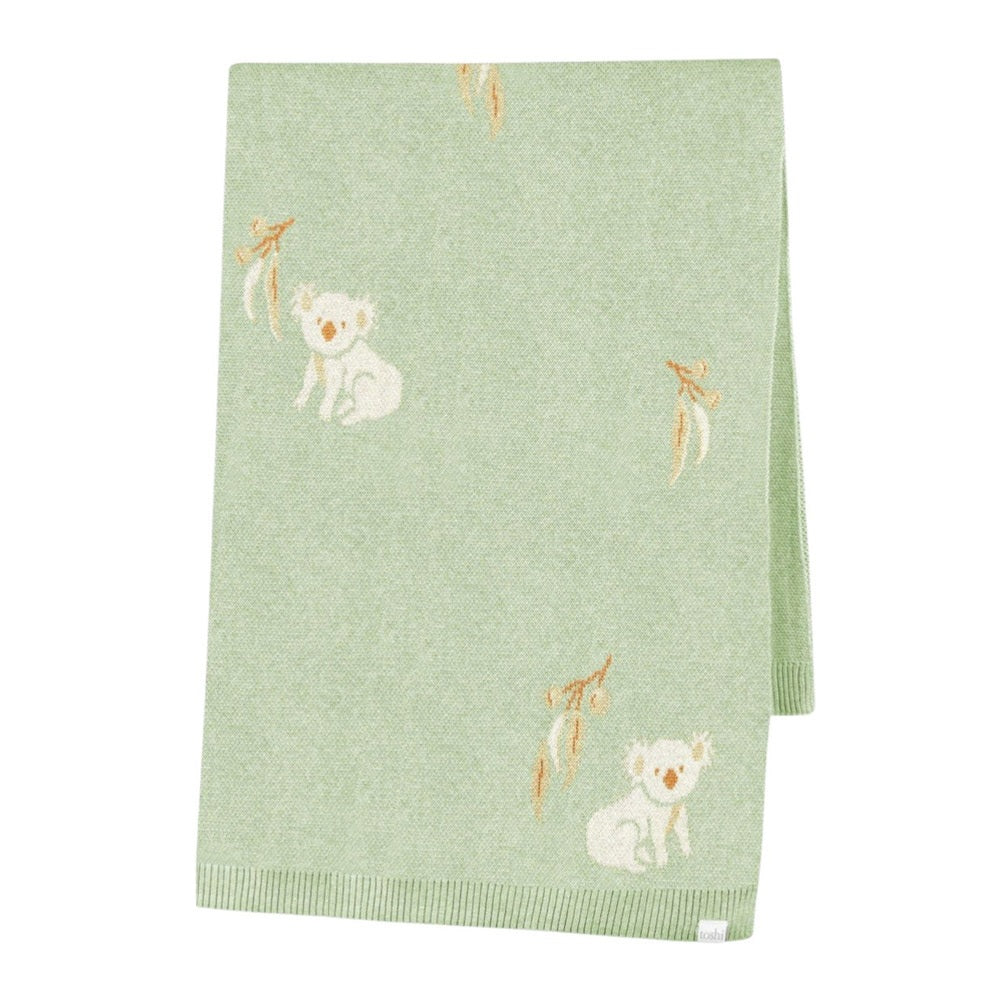 The Toshi Organic Blanket Storytime by Toshi is a soft, light green organic baby blanket with small white koala bear illustrations and leafy branches, shown neatly folded on a white background.