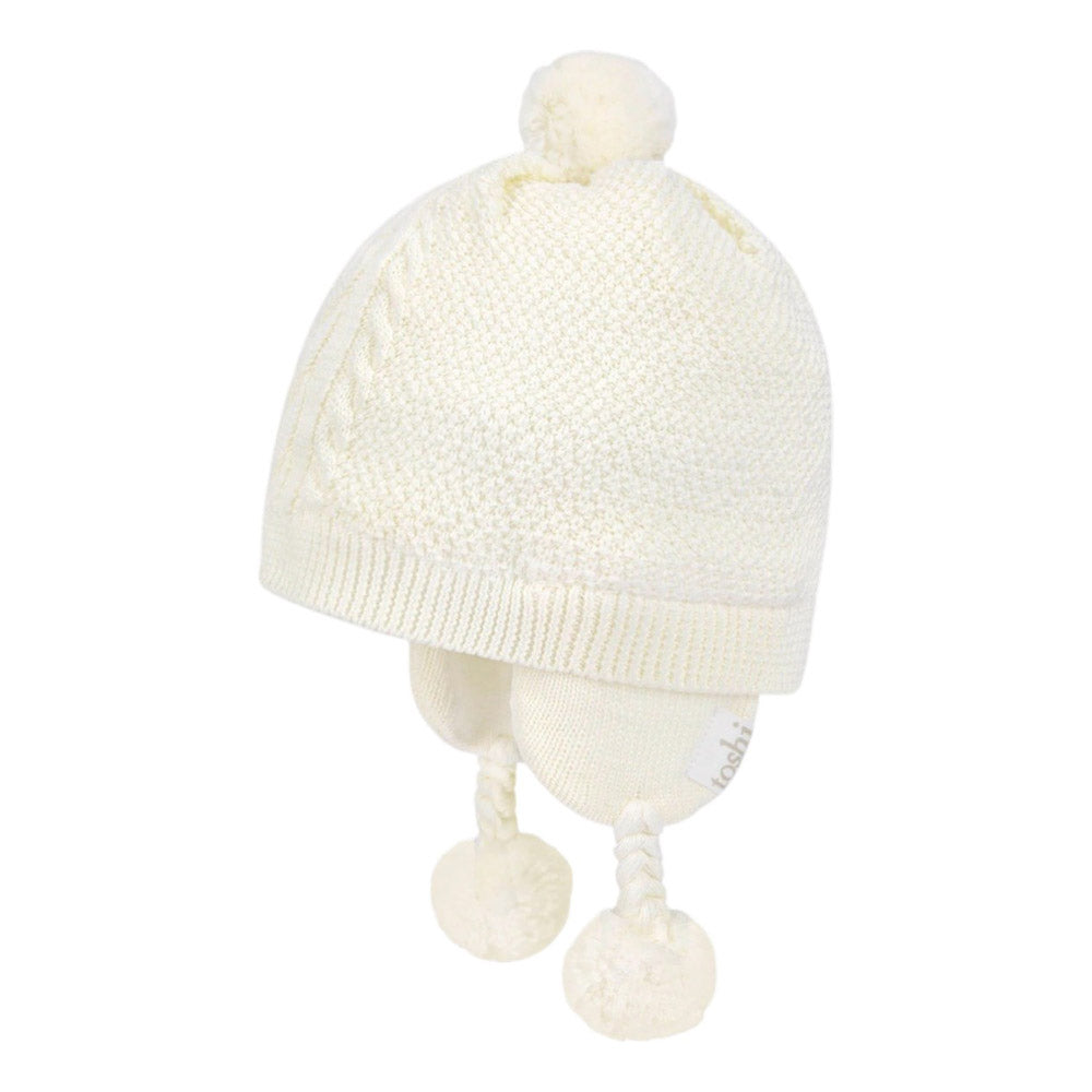 The Toshi Organic Earmuff Yummy Cream by Toshi is a soft, off-white knit winter hat with cozy ear flaps and matching pom-poms, designed for warmth and comfort.