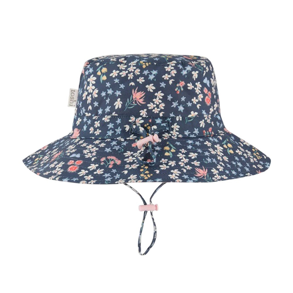 The Toshi Sunhat Acacia Midnight by Toshi is a blue cotton sun hat with a wide brim, colorful floral pattern, and an adjustable pink chin strap, providing children with UPF 50+ sun protection.