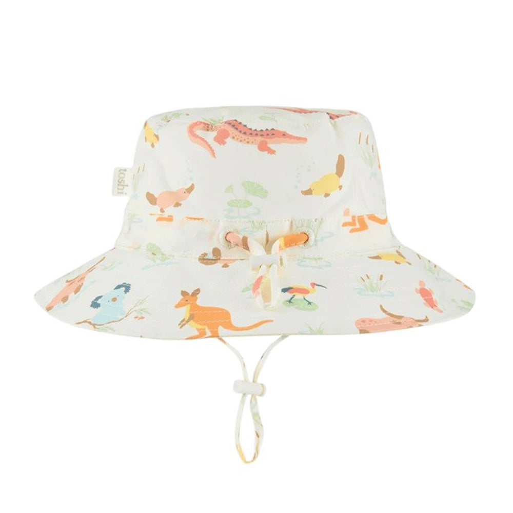 The Toshi Sunhat Banjo Kakadu Dawn by Toshi is a white kids’ hat with UPF 50+ protection, decorated with Australian animals such as kangaroos, crocodiles, and birds, and includes an adjustable chin strap for comfort.