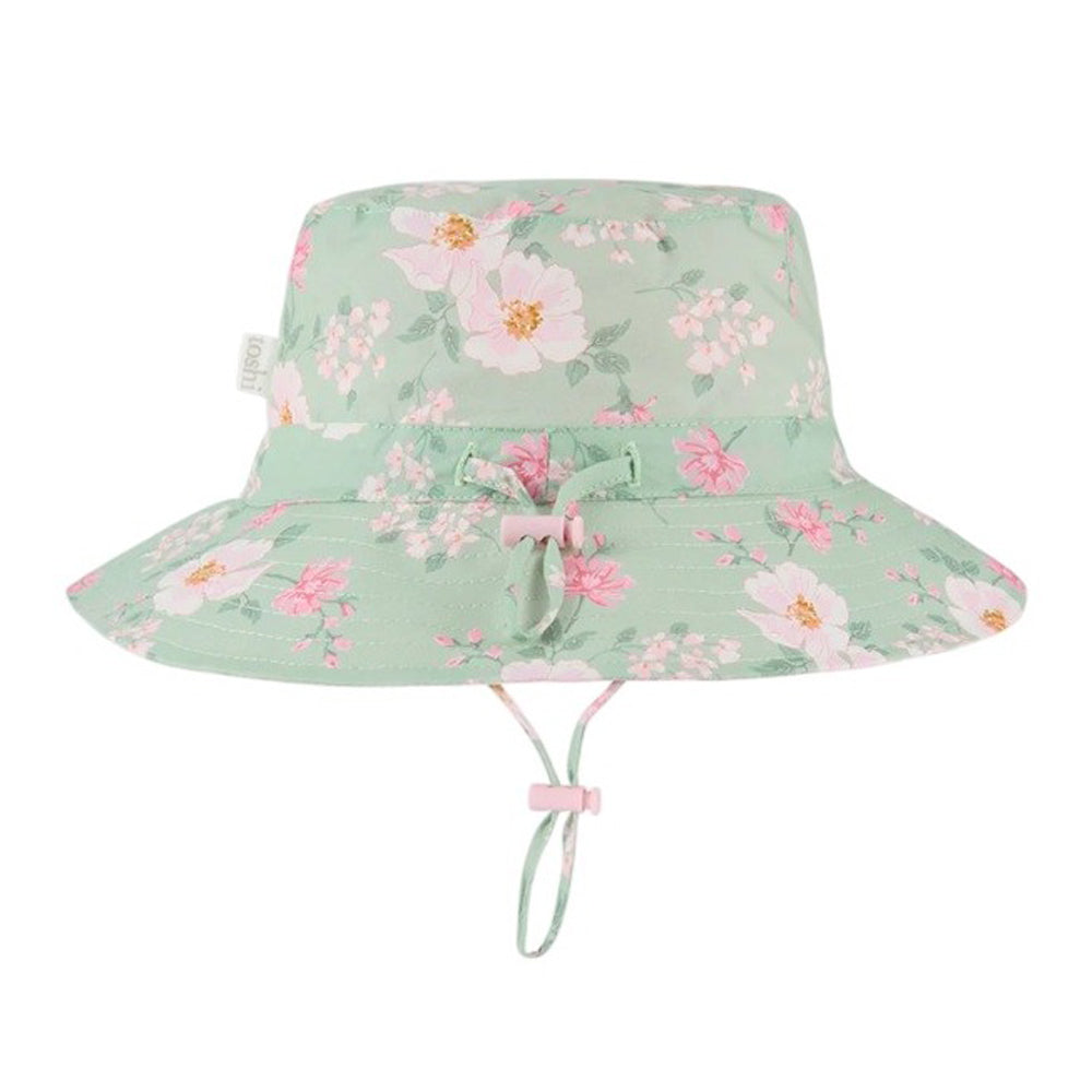 The Toshi Sunhat Desert Rose Apple by Toshi is a light green hat with a pink and white floral pattern, UPF 50+ protection, wide brim, front bow detail, and an adjustable chin strap.