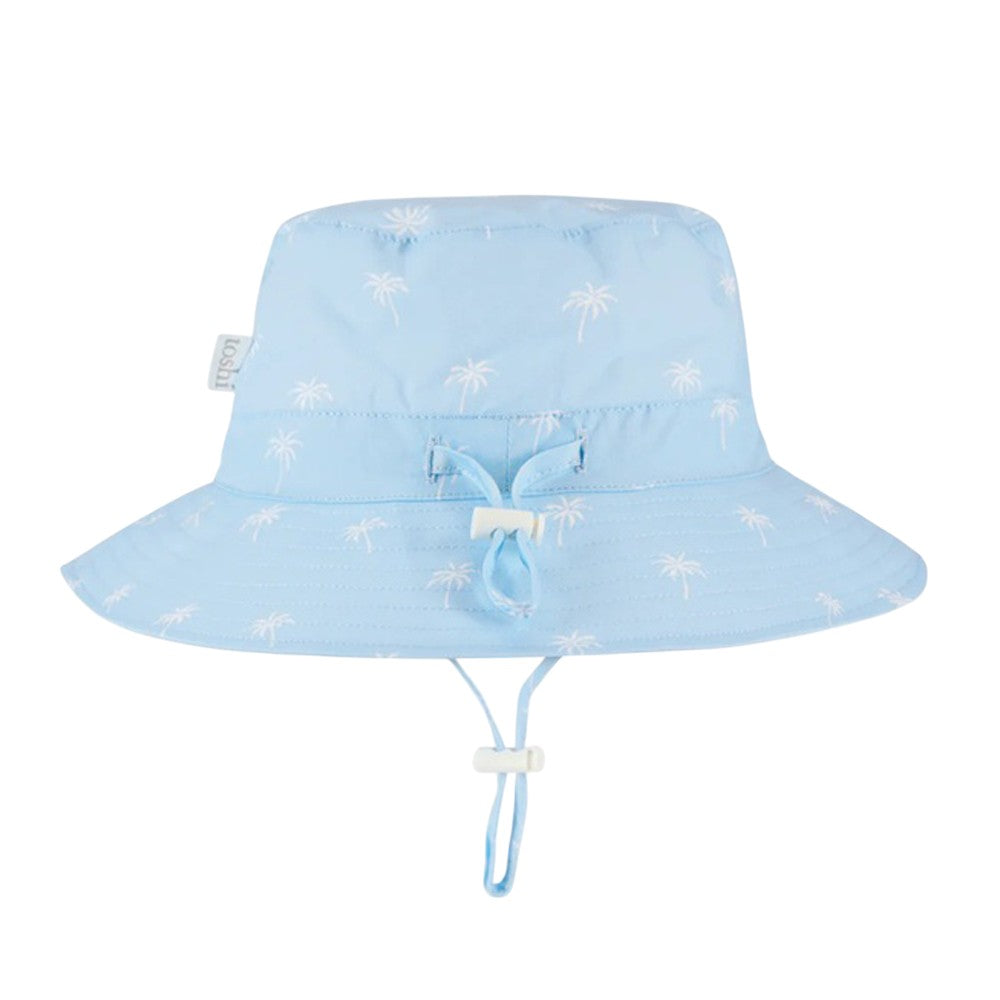 The Toshi Sunhat Spell Palm Sky by Toshi is a light blue children's cotton sun hat with white palm tree print, wide brim, adjustable chin strap, front drawstring for fit, and UPF 50+ protection for safe outdoor play.